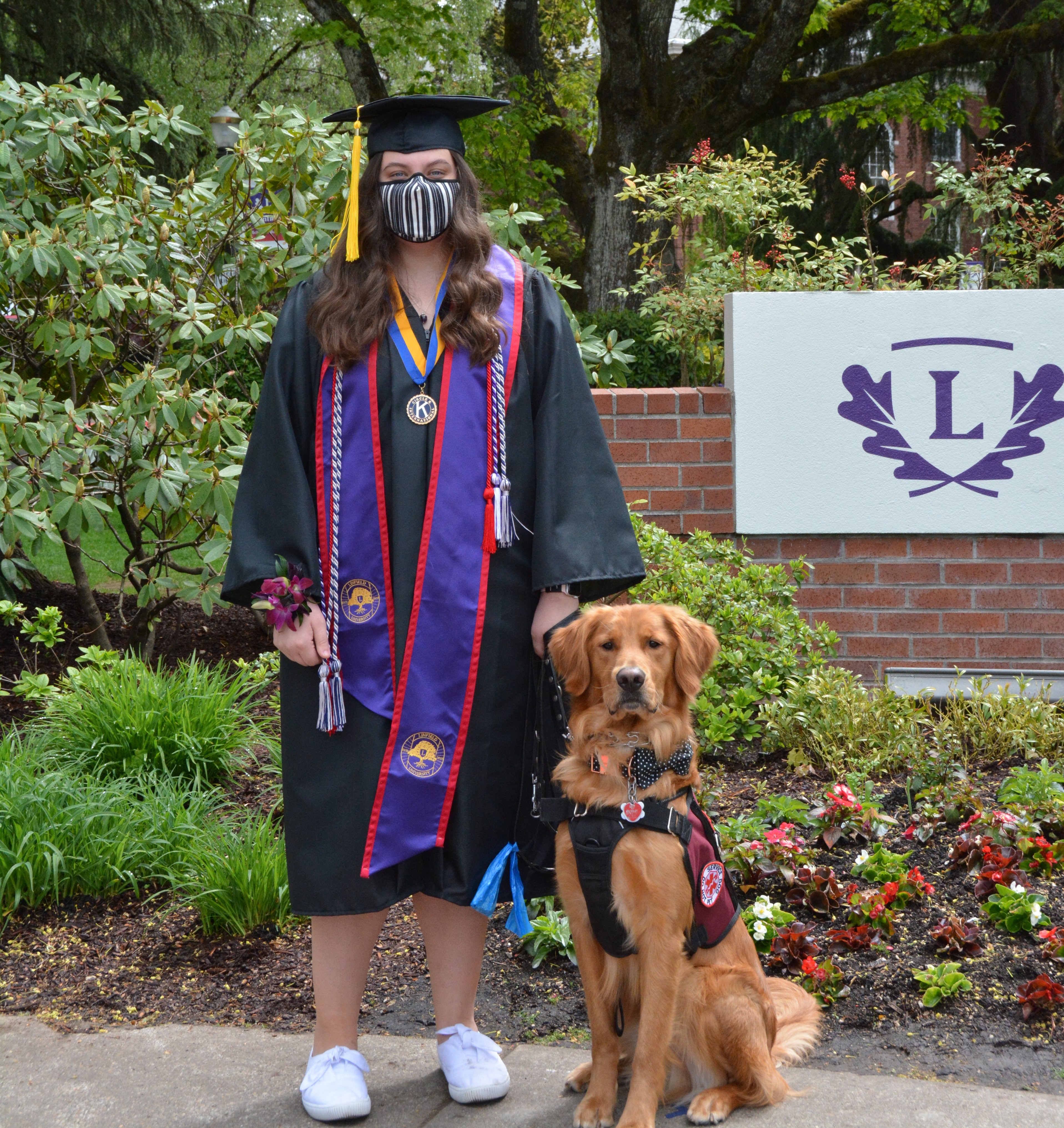 Image of Olivia in colorful graduation regalia. Her service animal is also in the picture