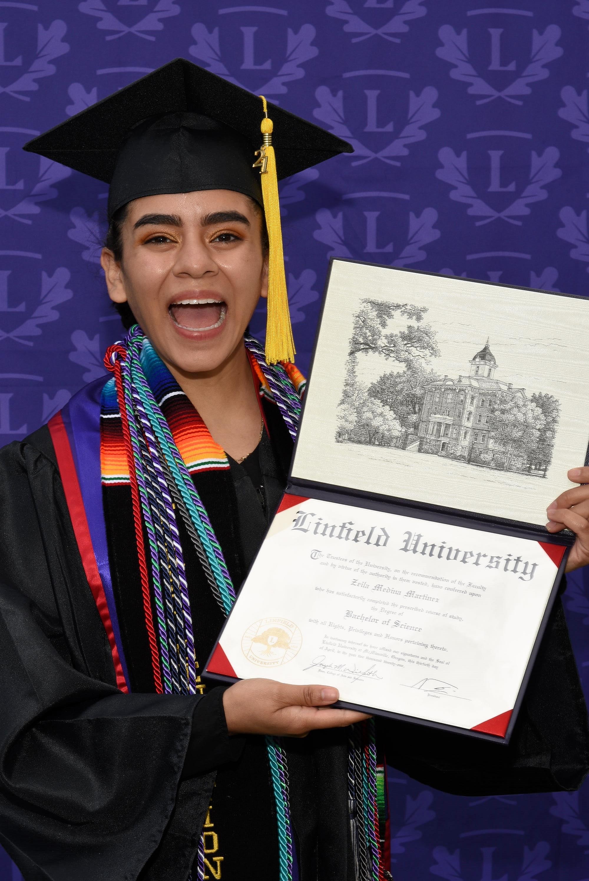 Zeila has a big smile on her face while displaying her Linfield diploma